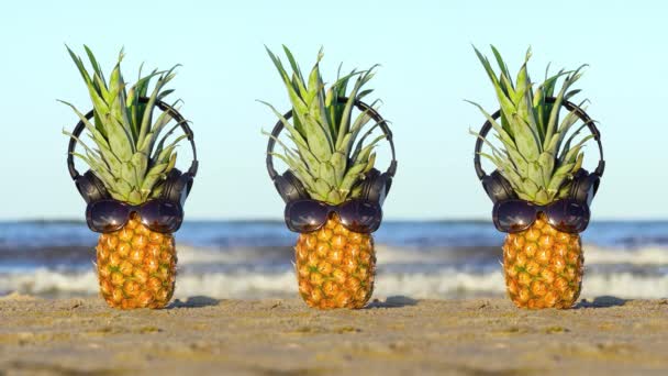 Deniz kumu üzerinde gözlüklü ve kulaklıklı ananas. — Stok video