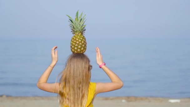 Το κορίτσι στην παραλία ισορροπεί έναν ανανά στο κεφάλι. — Αρχείο Βίντεο