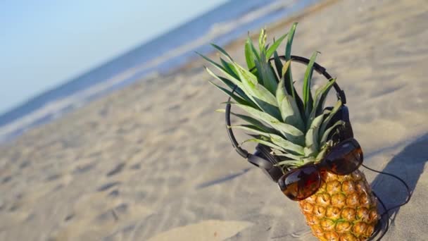 Słuchawki i gogle noszone na ananasie na plaży — Wideo stockowe