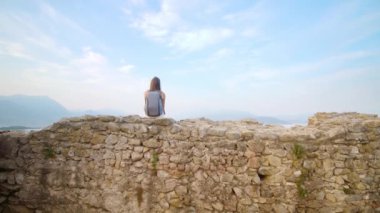 Tuğlaların üzerinde oturan kız Garda Gölü manzarasına bakıyor.