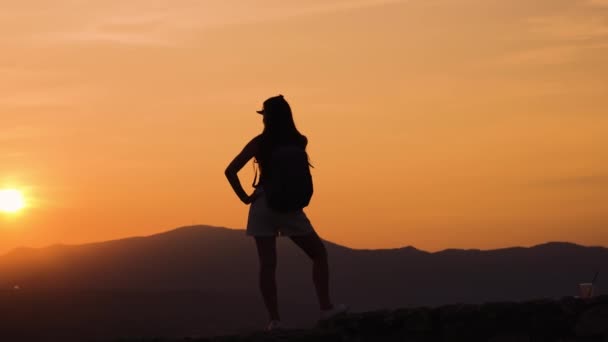 Η σιλουέτα του κοριτσιού που βλέπει το ηλιοβασίλεμα πάνω από τα βουνά — Αρχείο Βίντεο