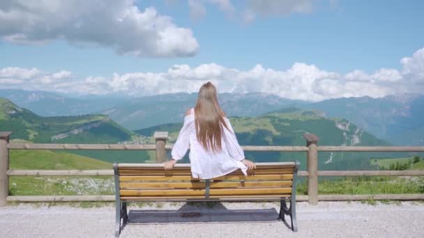 Девушка сидит на скамейке в зеленых горах — стоковое видео