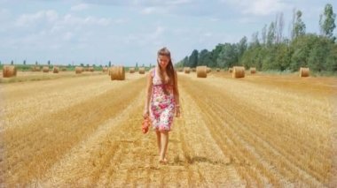 Kız tarlada samanlıklarla yürüyor.