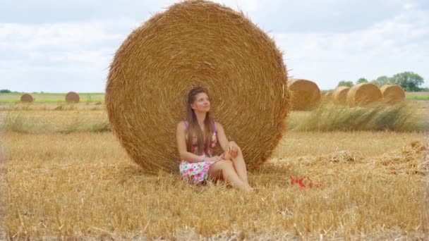 Vrouw zittend voor gele hooiberg op het zomerveld — Stockvideo