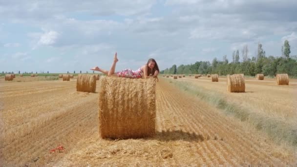 Meisje liggend op hooibal op het beteelde veld — Stockvideo