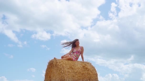 Lány ül a szénakazalban az ég hátterében — Stock videók