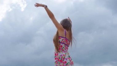 Gökyüzünün arka planında kollarını kaldırmış bir kız