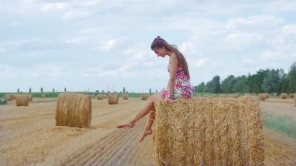 Meisje zit op de hooiberg beweegt haar voeten — Stockvideo