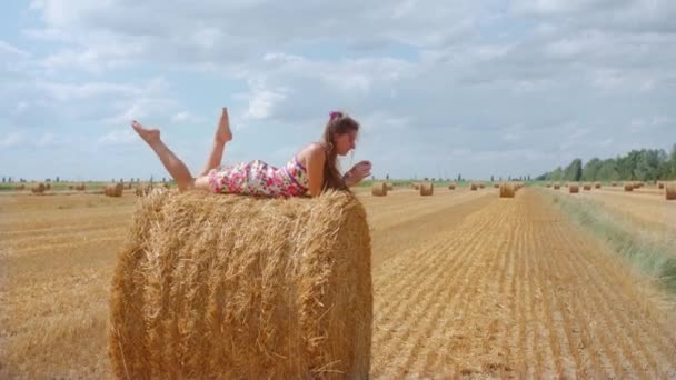 Meisje liggend op hooibal op zomer cultuurveld — Stockvideo