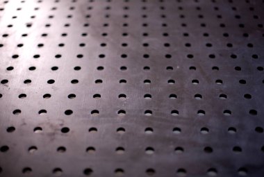 Birçok deliği olan bir metal tablonun kara yüzeyi.