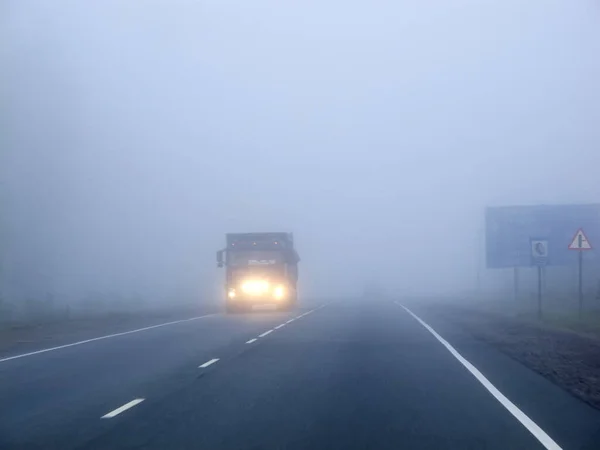 Cars in the fog. Bad weather and dangerous automobile traffic on the road. Light vehicles in fog.