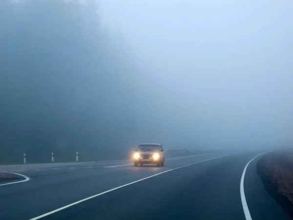 Cars in the fog. Bad weather and dangerous automobile traffic on the road. Light vehicles in fog.