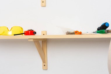 Duvara ahşap bir raf, gözlük ve mezura, vida ve koruyucu eldivenleri tamir etme süreci tahtada.