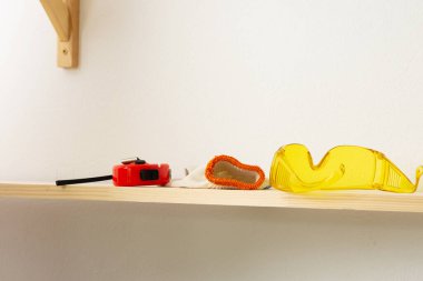 Duvara ahşap bir raf, gözlük ve mezura yerleştirme süreci, koruyucu eldivenler tahtada.