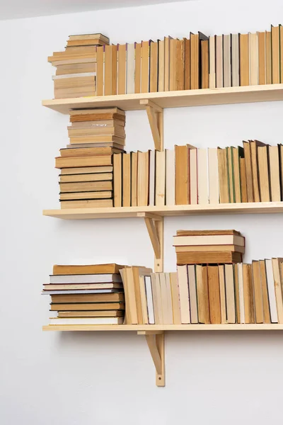 Light wooden bookshelves with hardback overturned books in white interior, home library