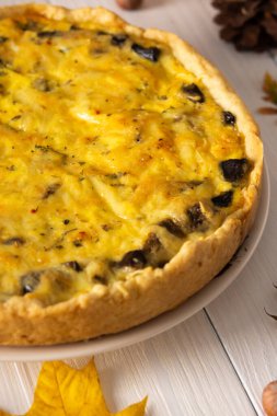 Mantarlı ve peynirli kiş turtası, sonbahar arkaplanı düşmüş akçaağaç ve meşe yaprakları, çam kozalakları ve fındıklı