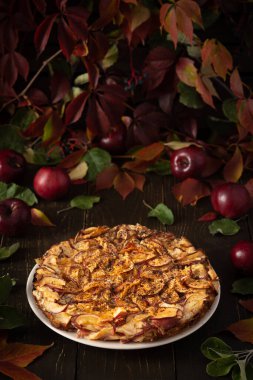 Kırmızı elmalı lezzetli turta, ahşap zemin üzerine kakao serpiştirilmiş elmalı turta, kırsal stil, kırmızı üzüm yaprakları ve olgun meyvelerden oluşan arka plan.