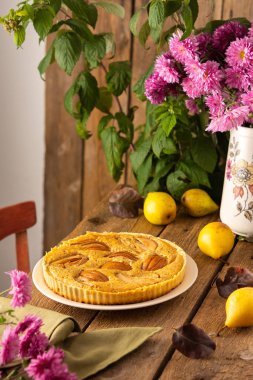 Ahşap zemin üzerinde sarı armuttan armut turtası, arka planda ahududu çalısı, vazoda pembe kasımpatı, kırsal tarzda.