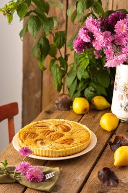 Ahşap zemin üzerinde sarı armuttan armut turtası, arka planda ahududu çalısı, vazoda pembe kasımpatı, kırsal tarzda.