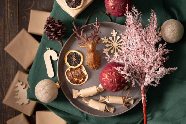 Noel veya yeni yıl arkaplanı, toplar ve ev yapımı şekerler, kurutulmuş meyveler ve dekoratif geyik, ladin ve pamuk rengi dallar yeşil masa örtüsü üzerinde, el işi kağıt hediyeler, üst manzara