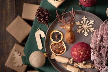 Noel veya yeni yıl arkaplanı, toplar ve ev yapımı şekerler, kurutulmuş meyveler ve dekoratif geyik, ladin ve pamuk rengi dallar yeşil masa örtüsü üzerinde, el işi kağıt hediyeler, üst manzara