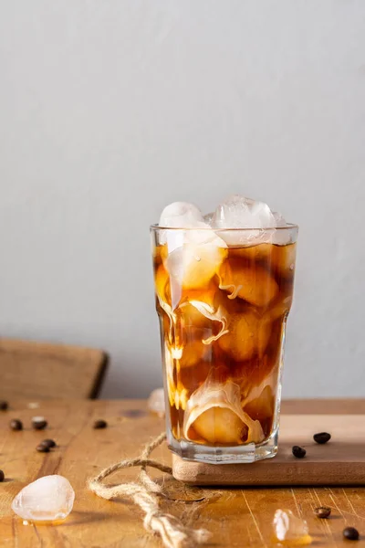 Soğuk serinletici kahve, buzlu ve kremalı bulutlar, bir bardakta, tahtaya yakın plan, kakao çekirdekleri masaya saçılmış.