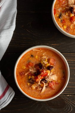 Fasulye ve mısır, domates ve tavuk göğsü, koyu ahşap arka planda bir kase çorba ve peçete.