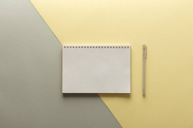 Gri ve sarı arkaplan üzerine açık spiral not defteri, defter ve kalem dokuma kağıdının üzerinde, düz konsept ise yılın sarı ve gri renklerinde.