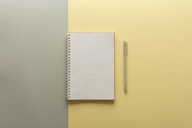 Gri ve sarı arkaplan üzerine açık spiral not defteri, defter ve kalem dokuma kağıdının üzerinde, düz konsept ise yılın sarı ve gri renklerinde.