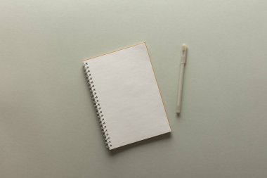 Gri zemin üzerinde spiral bir not defteri, defter ve kalem dokunun üzerine uzanır, yılın modaya uygun renklerinde düz konsept