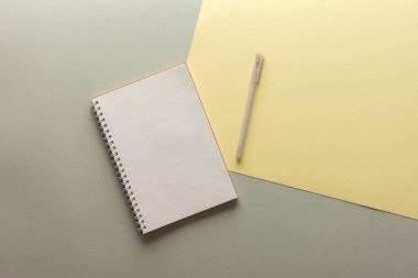 Gri ve sarı arkaplan üzerine açık spiral not defteri, defter ve kalem dokuma kağıdının üzerinde, düz konsept ise yılın sarı ve gri renklerinde.