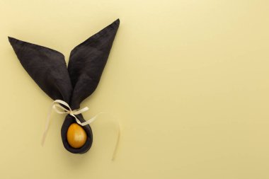 Sarı arka planda koyu gri peçeteden ve altın boyalı yumurtadan gelen soyut paskalya tavşanı, Paskalya bayramı konsepti