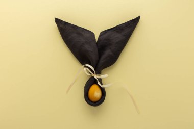 Sarı arka planda koyu gri peçeteden ve altın boyalı yumurtadan gelen soyut paskalya tavşanı, Paskalya bayramı konsepti