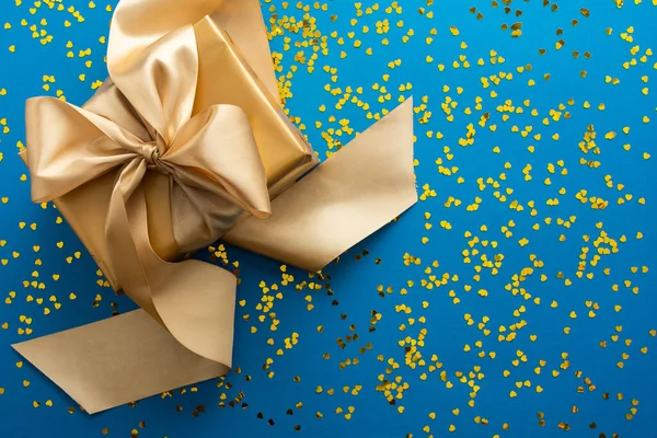 Pudełko Złotym Łukiem Niebieskim Tle Błyszczącymi Złotymi Sercami Koncepcja Urodzinowa — Zdjęcie stockowe