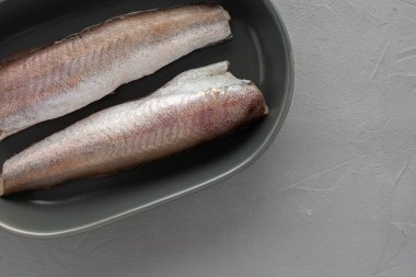 İki çiğ hake leşi, gri beton arka planda seramik bir kasede yakın plan.