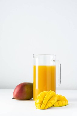 Beyaz arka planda cam bir sürahi içindeki mango suyu, doğranmış mango ve sağlıklı, lezzetli, tatlı doğal bir içecek.