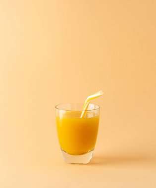 Lezzetli bir portakal suyu ya da bej arka planda izole edilmiş bir pipetle bardakta mango suyu.