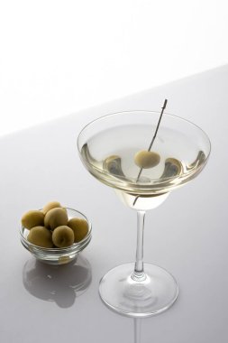 Gri arka planda zeytinli kokteyl bardağında vermut, hafif alkollü içecek.