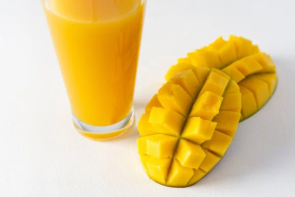 Mango juice in a glass with a straw on a white background, chopped mango fruit, delicious healthy sweet natural drink