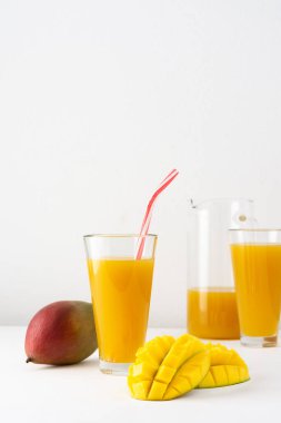 Bardakta mango suyu ve beyaz arka planda meyve suyu ve pipet, doğranmış mango ve lezzetli, sağlıklı, doğal bir içecek.