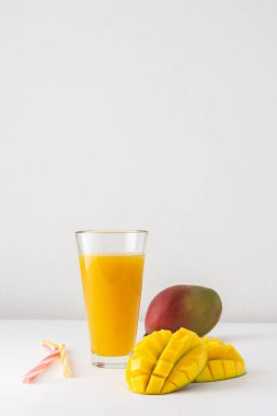 Meyve suyu bardaklarında mango suyu ve beyaz arka planda pipet, doğranmış mango ve lezzetli, sağlıklı, doğal bir içecek.
