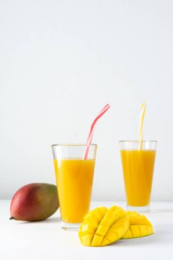 Meyve suyu bardaklarında mango suyu ve beyaz arka planda pipet, doğranmış mango ve lezzetli, sağlıklı, doğal bir içecek.