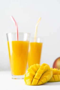 Meyve suyu bardaklarında mango suyu ve beyaz arka planda pipet, doğranmış mango ve lezzetli, sağlıklı, doğal bir içecek.