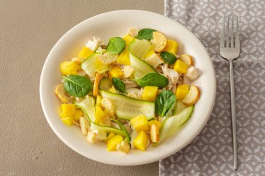 Kahverengi zemin üzerinde salata ve çatal yakın çekim tabağı, salatalık ve tavuk göğsü salatası, mozzarella ve tatlı mango parçaları ve ıspanak ile kızarmış ekmek.