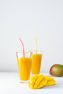 Meyve suyu bardaklarında mango suyu ve beyaz arka planda pipet, doğranmış mango ve lezzetli, sağlıklı, doğal bir içecek.