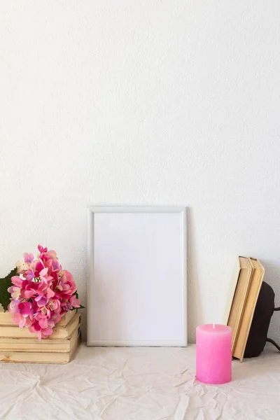 Home decor mock-up, blank picture frame near white painted concrete wall ,a branch of pink hydrangea on old books and a candle