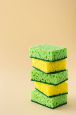 Tarafsız bej arka planda yeşil ve sarı bulaşık süngeri yığını, mutfak ve temizlik konsepti