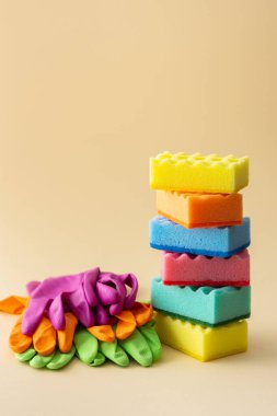 Tarafsız bej arka plan, mutfak ve temizlik konsepti üzerine bir yığın renkli bulaşık süngeri ve lastik eldiven.