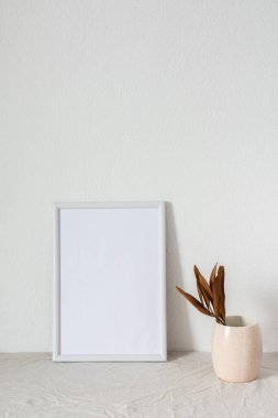 Dekor mokasyonu, beyaz boyanmış beton duvarın yanındaki boş resim çerçevesi, kuru yapraklı dallar.