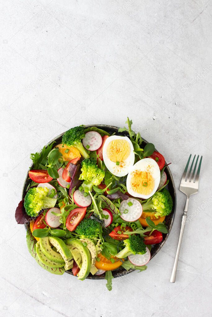 Delicious light breakfast, salad with tomatoes and radishes, avocado and boiled eggs, top view